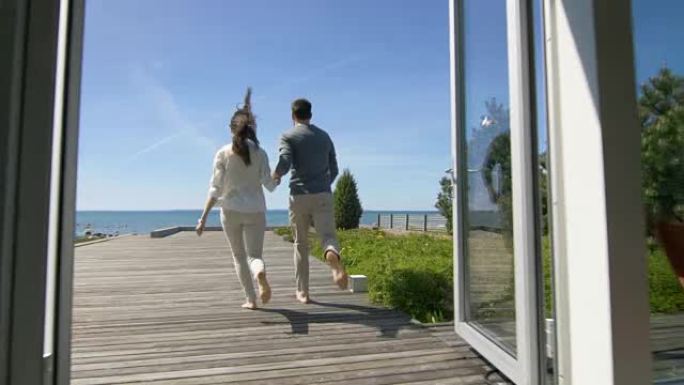 幸福的年轻夫妇牵着手跑出家门，走到海边的露台上。