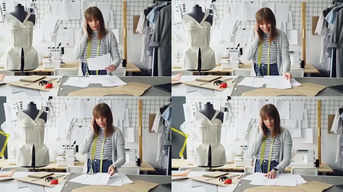 年轻有魅力的裁缝师正在手机上讨论服装设计，并在她的工作室里用衣服在假人和铁轨之间工作时检查草图。