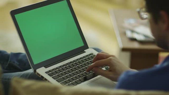 男子躺在沙发上，在家中使用带有绿屏的笔记本电脑