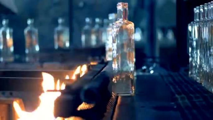 玻璃瓶在传送带上用火加热以进行巴氏杀菌。4K。