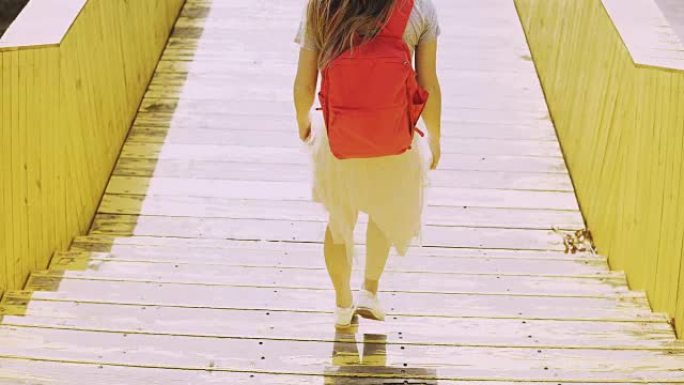 长发的女人走在城市的桥上。红色背包的欧洲女孩。黄色城市走道墙。4K