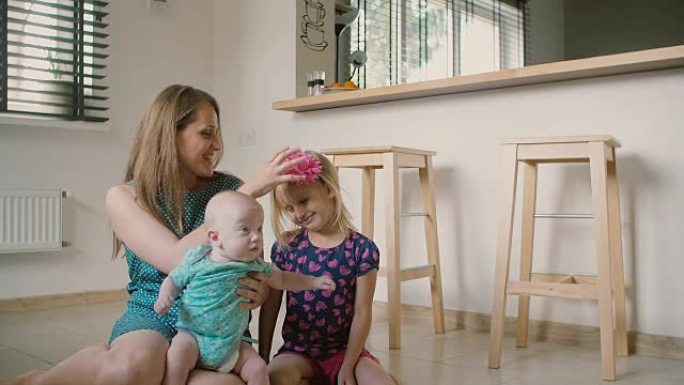美丽的年轻母亲和她的宝贝儿子和可爱的小女儿坐在厨房地板上。慢动作