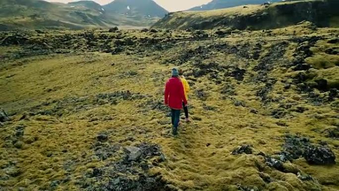 鸟瞰图，两名女性行走在覆盖着苔藓的火山岩上，在冰岛探索草地。游客一起徒步旅行