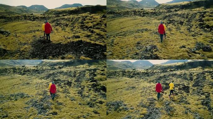 鸟瞰图，两名女性行走在覆盖着苔藓的火山岩上，在冰岛探索草地。游客一起徒步旅行
