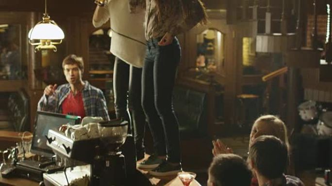 两个女孩在桌子上喝酒跳舞，而每个人都在酒吧里玩得很开心。