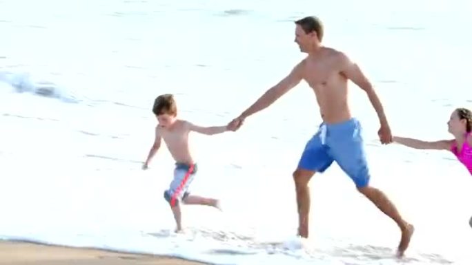 父亲和两个孩子在沙滩上冲浪在沙滩上奔跑