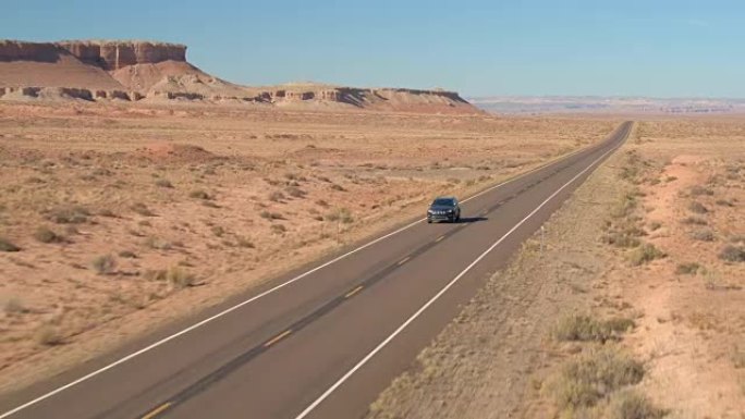 空中黑色SUV汽车在空旷的道路上行驶，穿越广阔的沙漠山谷