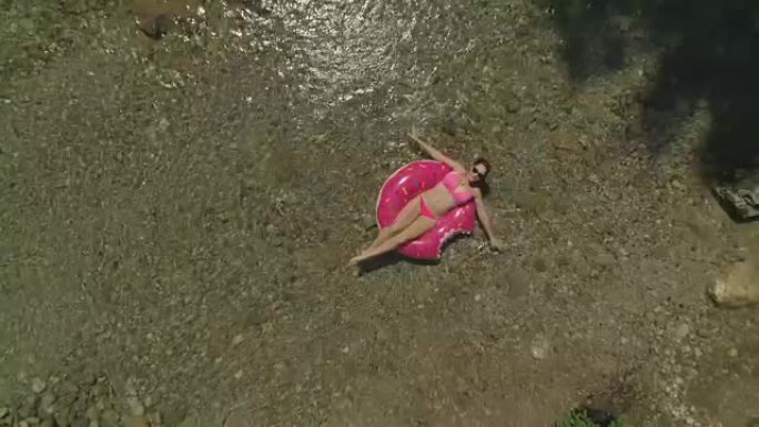 双臂扫过水面的空中女孩在甜甜圈漂浮的河边放松
