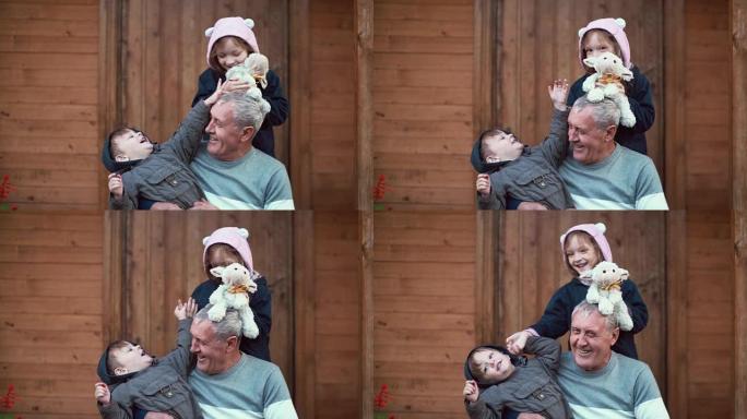 男孩坐在祖父的膝盖上，女孩站在后面拥抱。兄妹玩玩具羊，笑。4K