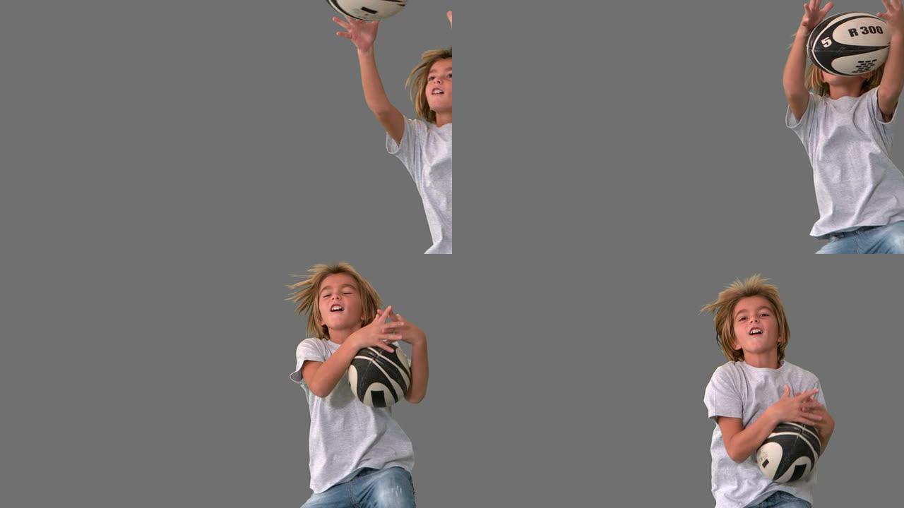 男孩在灰色背景上跳跃和捕捉橄榄球球