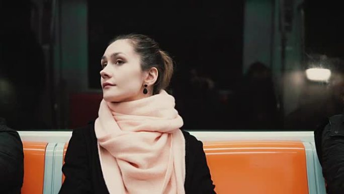 坐在地铁里年轻体贴的女人的肖像。女孩使用公共交通工具，环顾四周，看着窗户
