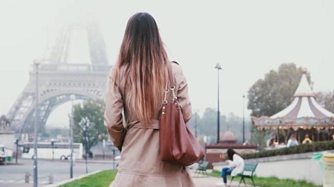 穿着法国风格的年轻女子步行到法国巴黎的埃菲尔铁塔。女孩看着著名的景象