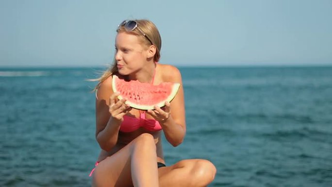 迷人的金发女人在海滩上吃西瓜