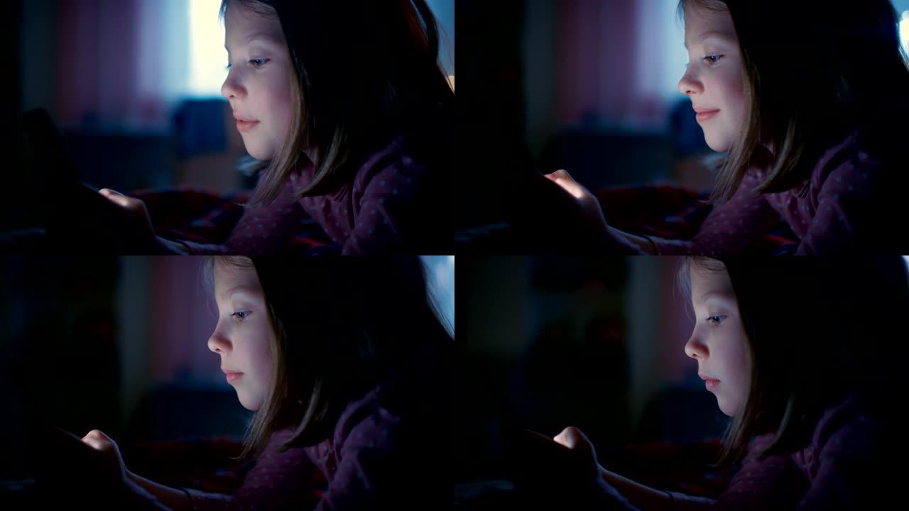 可爱的小女孩晚上在她的房间里，躺在床上使用智能手机。屏幕照亮了她的脸。