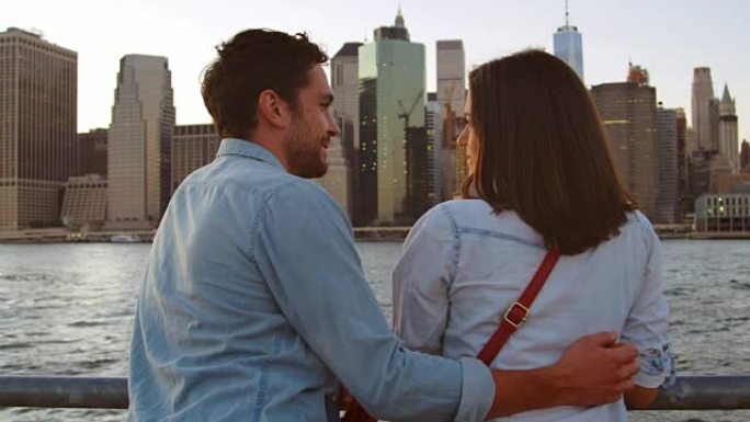 一对年轻夫妇在曼哈顿河边聊天，后景