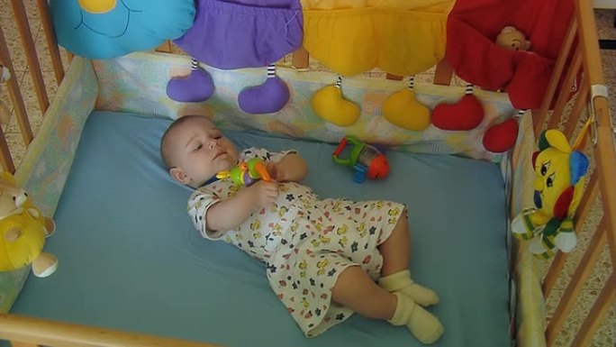 婴儿躺在婴儿床上，手里拿着一个玩具
