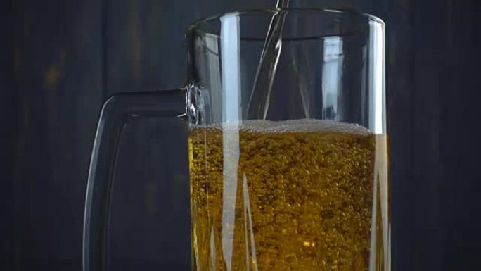 将啤酒倒入深色木制背景上的玻璃中。慢动作