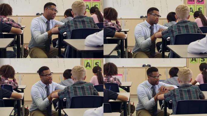 老师跪下帮助一个男孩坐在办公桌前，在R3D上拍摄