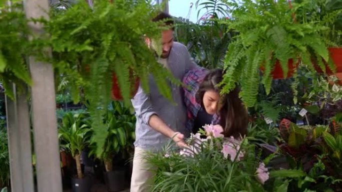 一对快乐的年轻夫妇在植物园里拥抱着对方，一个女人在闻着美丽的花朵