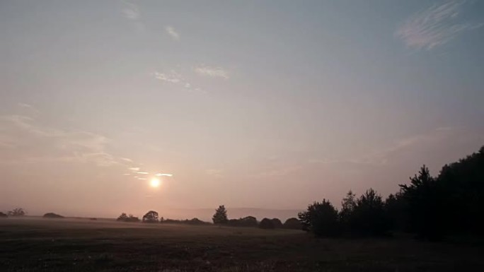 日出时的乡村场景，薄雾慢慢远离草地。太阳升起时会更加明亮。延时