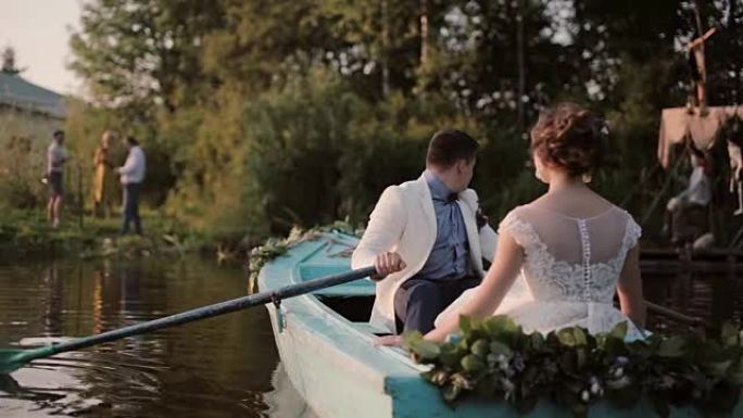 恋人在结婚那天玩得很开心。一对恋爱在一艘停泊在河岸的蓝色船上。新郎桨