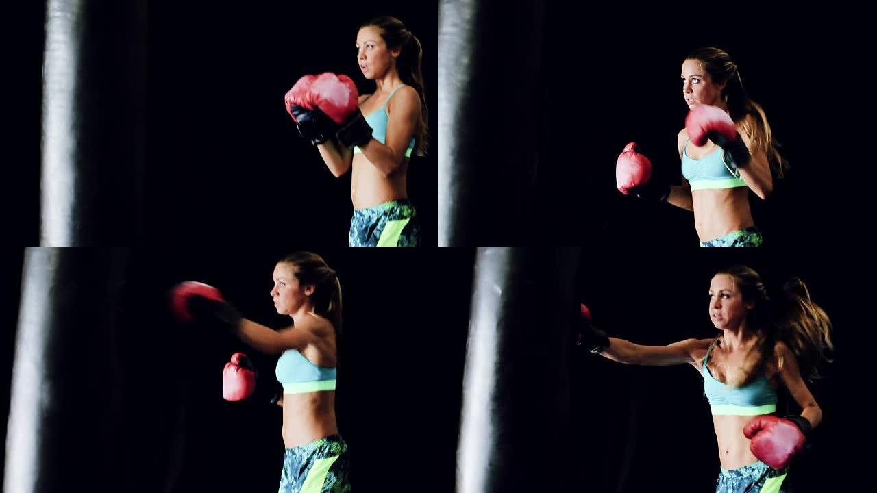 美丽强壮的年轻女拳击手训练与红色手套上的黑衣袋