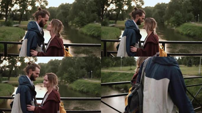 年轻的幸福夫妇在日落时与河一起在公园散步。美丽的男人和女人拥抱，在桥上说话