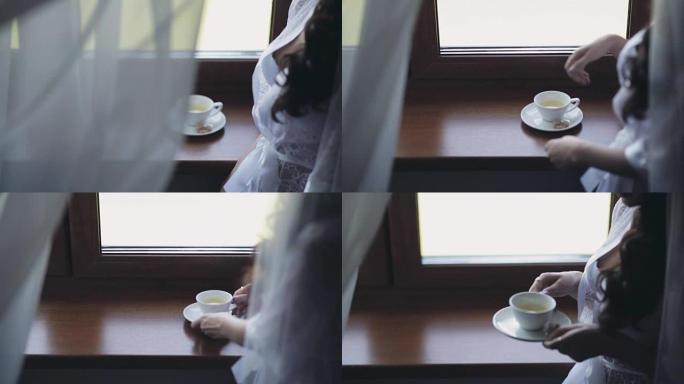 穿着优雅白色内衣的年轻女子的特写镜头，peignoir呆在窗户附近喝茶