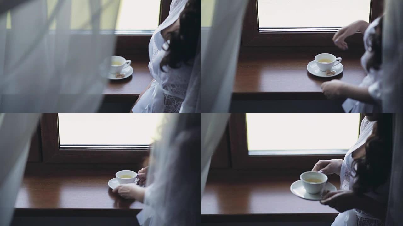 穿着优雅白色内衣的年轻女子的特写镜头，peignoir呆在窗户附近喝茶
