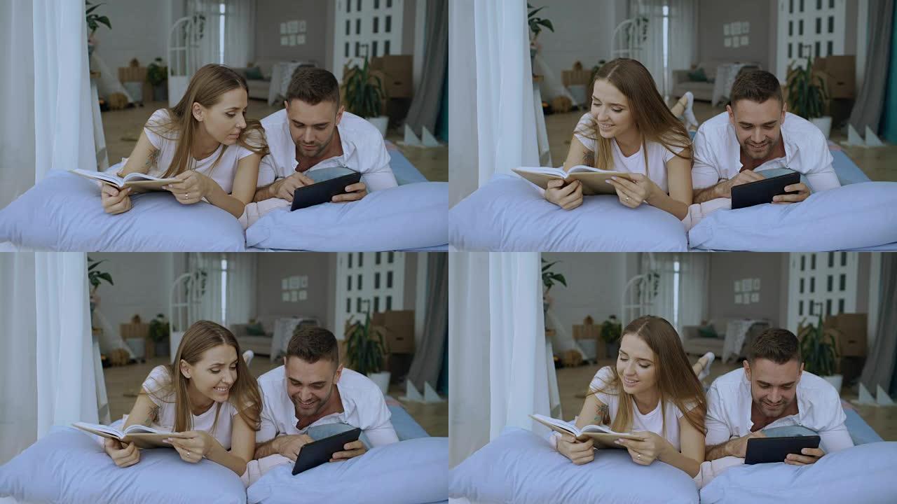 英俊的年轻人使用平板电脑显示平板电脑上的照片给他的女朋友读书和躺在家里的床上