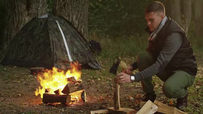 穿着秋衣的短发男子正在用斧头砍柴并将其扔进火中。
