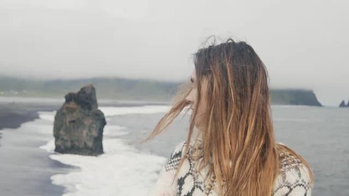 美丽悲伤的女人在冰岛的黑海滩上思考，巨魔脚趾在背景上摇摆不定