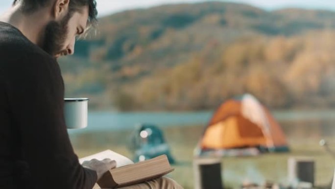 男子在露营旅行中坐着，喝咖啡和看书