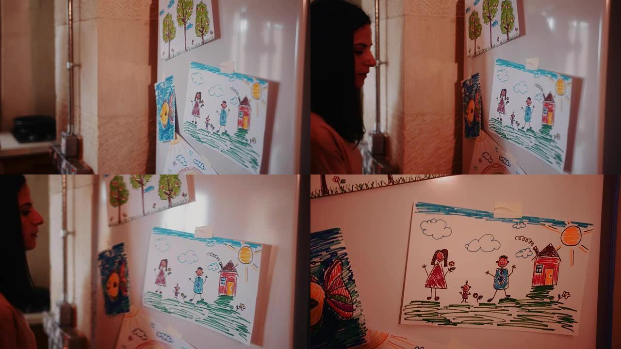 年轻的母亲在厨房里用儿童图画打开冰箱门