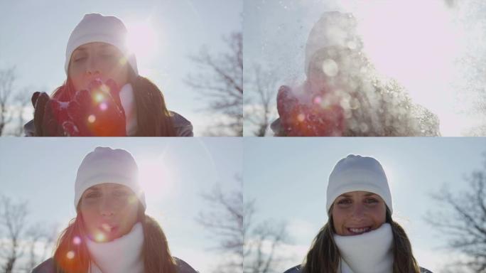 慢动作: 开朗的年轻女子将雪花吹入相机