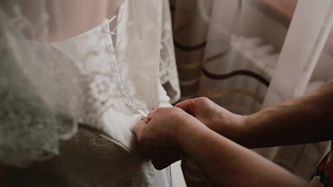女手帮助新娘穿上衣服的特写镜头。母亲为女儿系婚纱。后视图