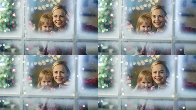 在圣诞节前夕，母女俩透过白雪皑皑的窗户，对着镜头挥手致意。圣诞Lites在窗户上闪闪发光。