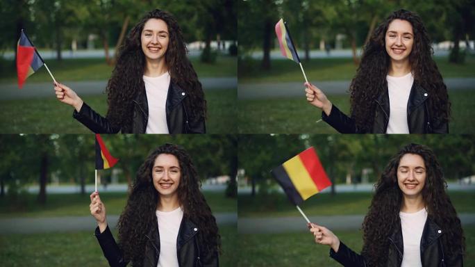夏天，迷人的女孩世界旅行者挥舞着比利时国旗，看着相机，微笑着站在绿色公园的慢动作肖像。人和旅游概念。