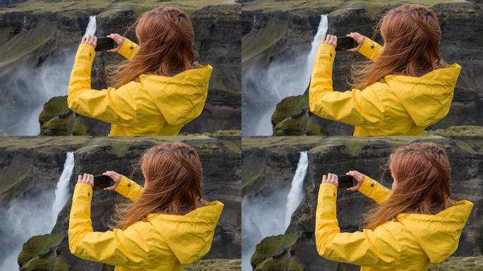 女人站在悬崖上，用智能手机拍摄瀑布的照片