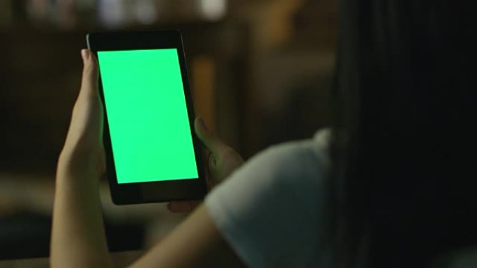 十几岁的女孩在晚上在风景模式下使用绿屏平板电脑。休闲生活方式。