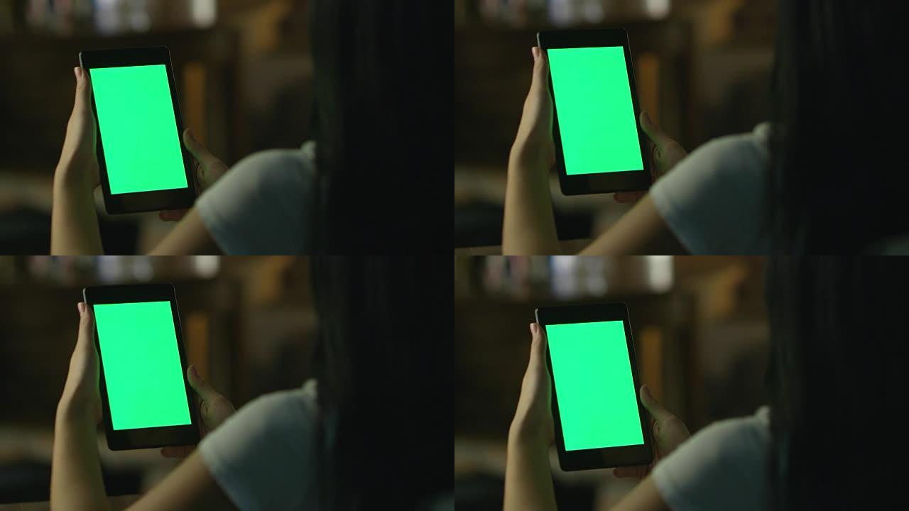 十几岁的女孩在晚上在风景模式下使用绿屏平板电脑。休闲生活方式。
