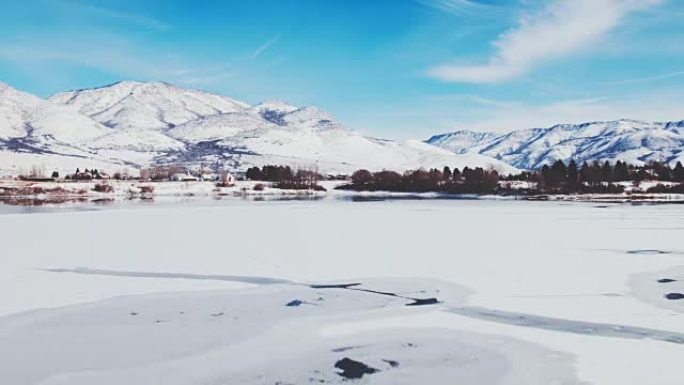 鸟瞰图飞越冬季湖，冰雪覆盖，背景为雪山