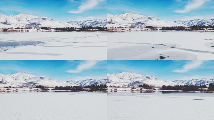 鸟瞰图飞越冬季湖，冰雪覆盖，背景为雪山