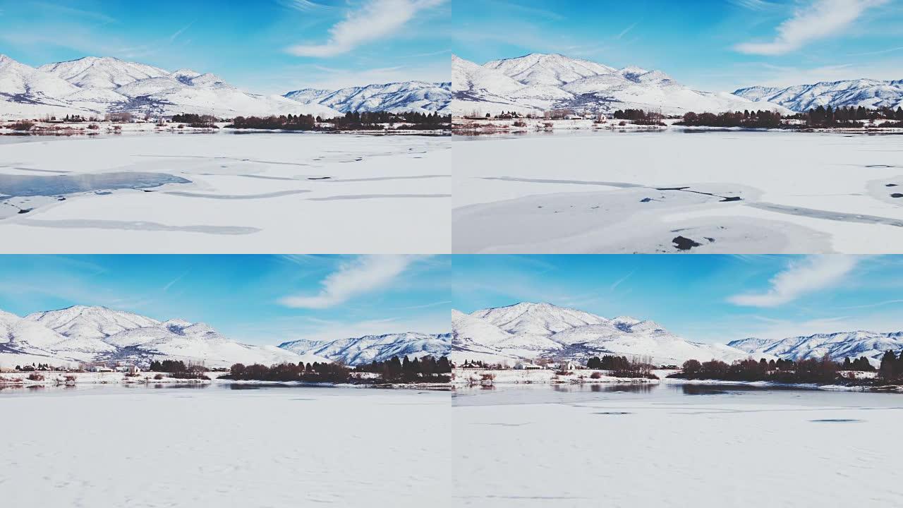 鸟瞰图飞越冬季湖，冰雪覆盖，背景为雪山