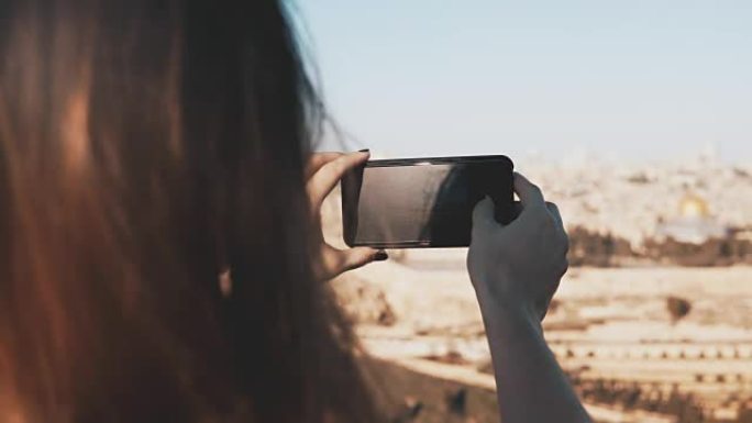 女孩拍摄以色列耶路撒冷的智能手机照片。阳光明媚的日子里，女性双手握着电话。捕捉瞬间。4K
