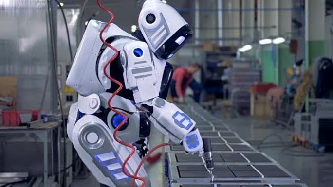 类似人类的机器人正在工厂中使用钻头