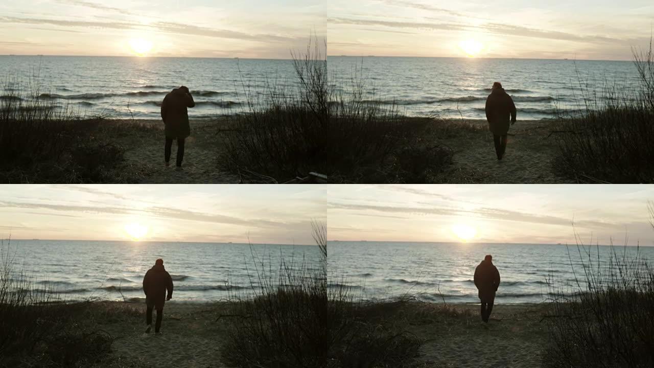 日落时分，年轻人在海边散步。孤独的男性在寒冷的日子里独自在海滩上度过时光