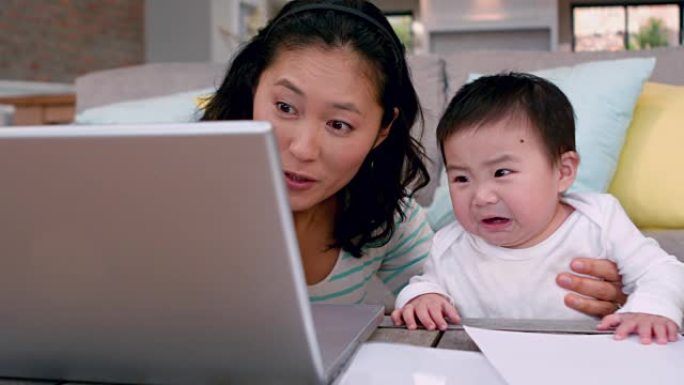 妈妈和哭闹的婴儿使用笔记本电脑