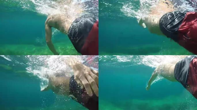 水下: 活跃的年轻人，纹身在海洋中的岩石海底上游泳