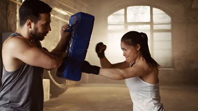 运动女子在伴侣/教练拿着的出气筒上训练拳头。她是职业拳击手，在铁杆健身房锻炼身体。